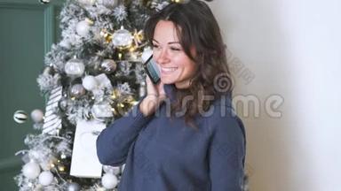 在<strong>圣诞</strong>树的背景下，用手机拍下迷人的深色头发的自拍